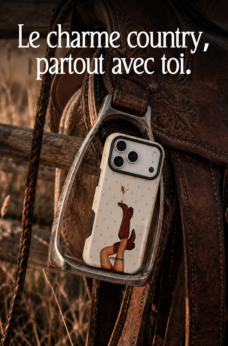 A clear phone case with a western-themed print of a woman's legs in cowboy boots and a horseshoe, hanging from a leather saddle on a rustic wooden fence. The image has French text overlay at the top: 'Le charme country, partout avec toi.