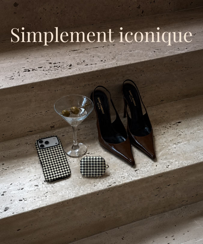A styled flat-lay on stone steps featuring a pair of pointed-toe slingback heels in glossy brown and black, alongside a black-and-white houndstooth phone case, a matching AirPods Cases, a martini glass, and a smartphone. The text 'Simplement iconique' appears at the top.