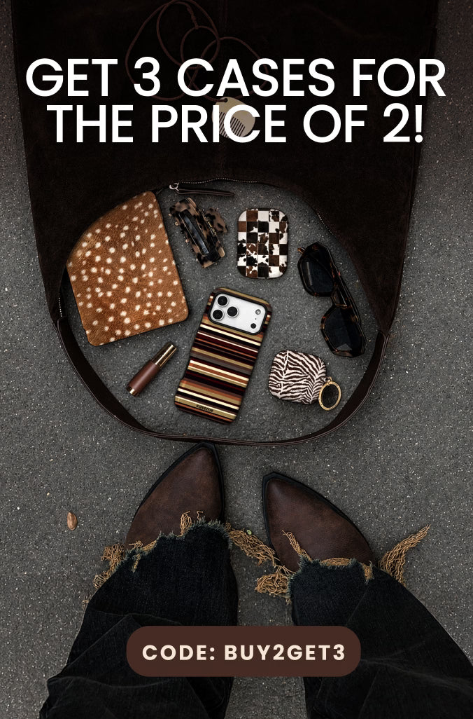 Promotional graphic showing an open dark brown leather suitcase on gray pavement with various accessories inside, including a patterned clutch, sunglasses, a striped phone case, and a small wallet. Large white French text reads 'ACHÈTE 2 ÉTUIS ET OBTIENS LE 3E GRATUITEMENT' with a brown label at the bottom reading 'CODE: BUY2GET3'.