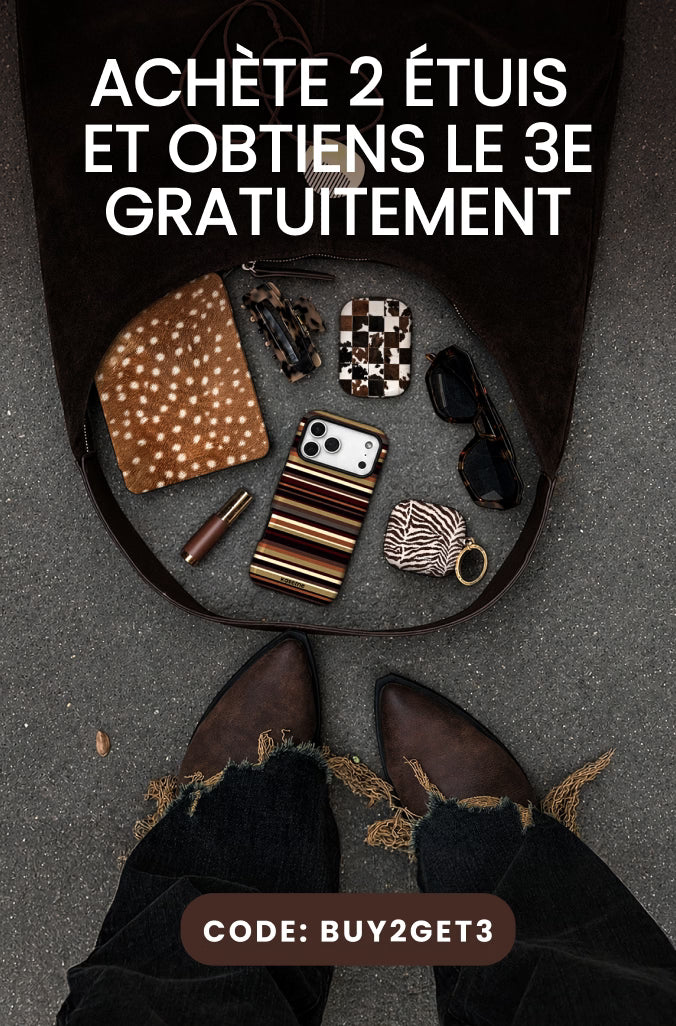 Promotional graphic showing an open dark tote bag laid on gray pavement, containing a patterned clutch, striped phone case, sunglasses, and small accessories. Large French text reads 'ACHÈTE 2 ÉTUIS ET OBTIENS LE 3E GRATUITEMENT' with a code banner at the bottom and visible boots/jeans and feet at the bottom edge, indicating a lifestyle promotional scene.