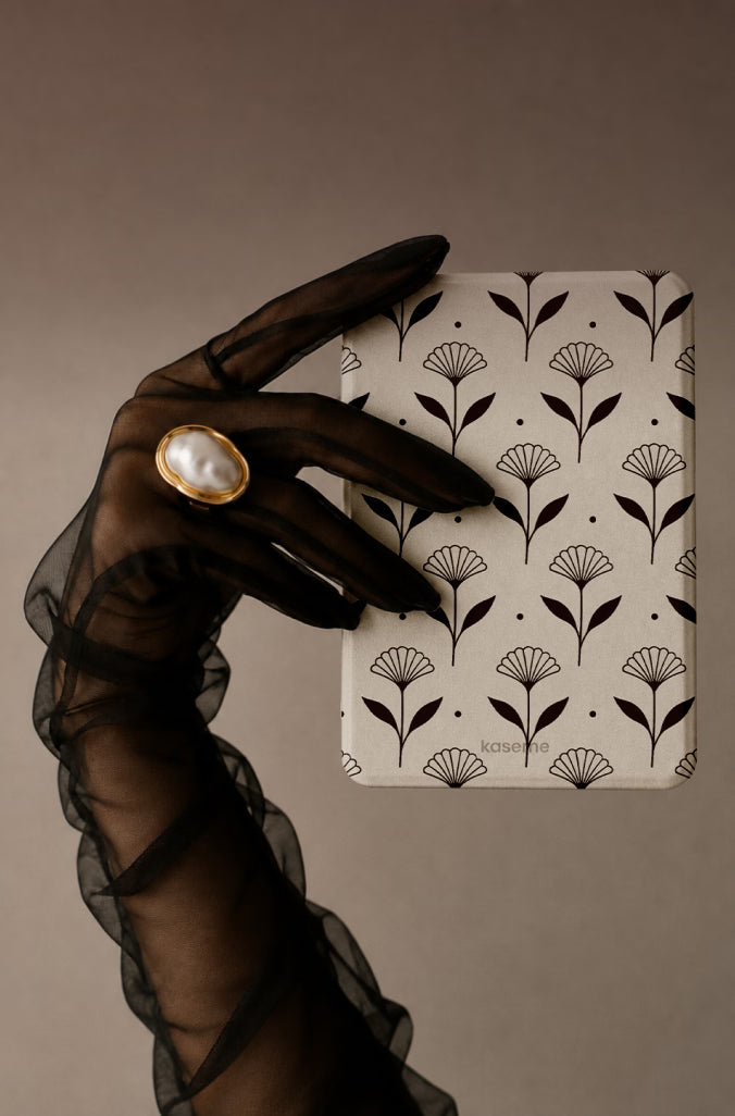 A hand wearing a sheer black ruffled glove holds a  E-Reader Cases with a white cover decorated with a black botanical fan pattern. The hand is adorned with a large oval ring featuring a white pearl and gold bezel.