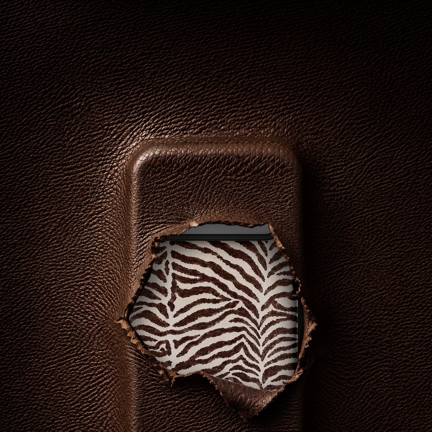 A close-up of dark brown textured leather with a torn opening revealing a white and brown zebra-patterned fabric underneath.