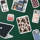 A collage of various phone cases and matching accessories arranged on a dark green background. The designs include a brown and beige cow print, a red gingham pocket case with white AirPods peeking out, a black and white polka dot laptop skin, floral patterns, and other retro-themed prints.